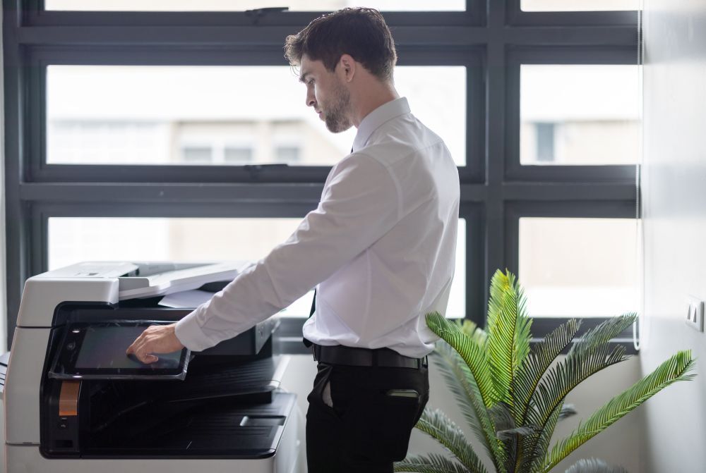 Hombre con camisa blanca usando el panel táctil de una impresora en una oficina.