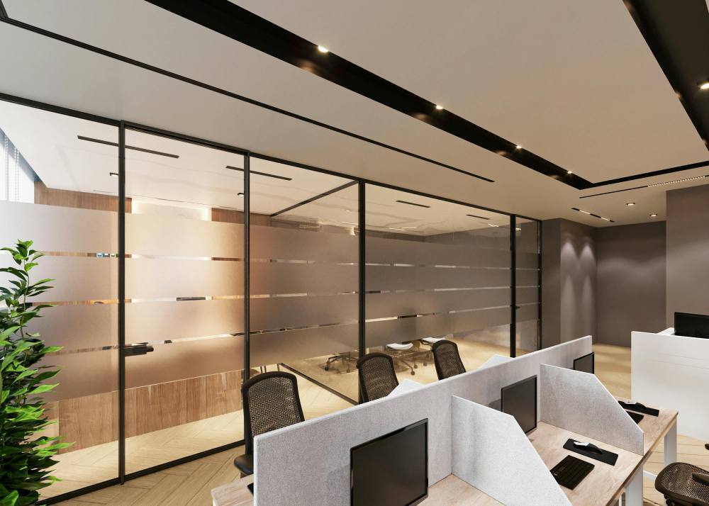 Puestos de trabajo modernos con paneles acústicos y sala de reuniones acristalada en una oficina híbrida corporativa.
